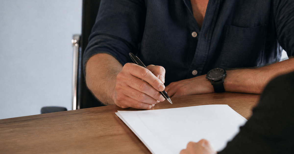 Vendeur signant document avec stylo, main suspendue au-dessus