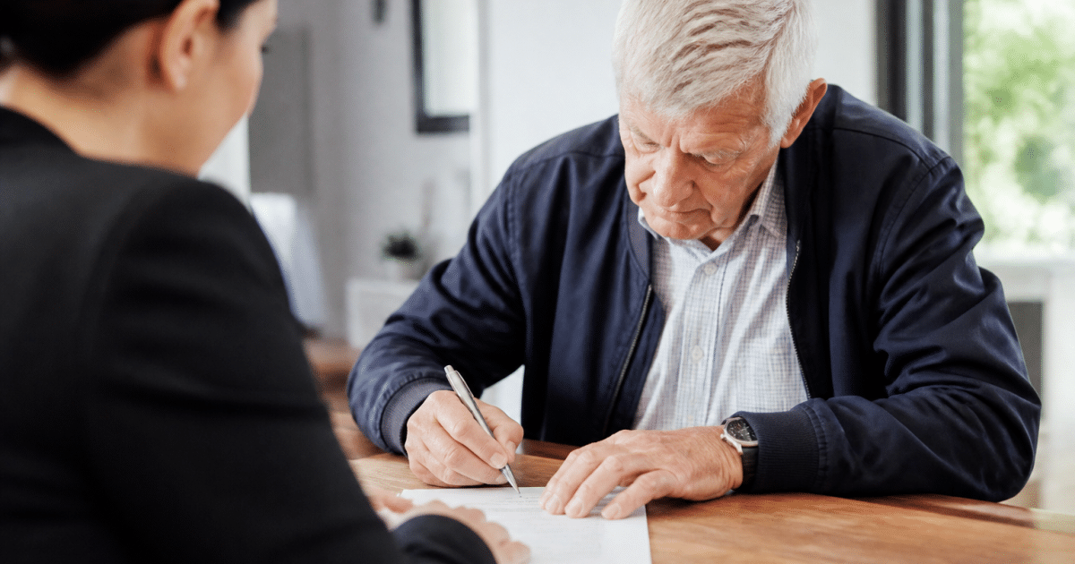 Personne agee signant un document immobilier avec agent assis